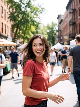 Cheerful young woman laughing on a busy city street market. Candid portrait of a happy female looking back in a red t-shirt