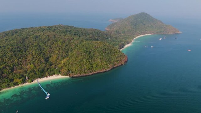 Lush green hills meet crystal blue ocean water on the coast of Phuket Thailand where a small boat rests near the sandy beach during a bright sunny afternoon