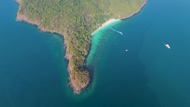 Clear blue waters surround green tropical islands in Phuket Thailand where boats anchor near white sandy beaches on a bright summer afternoon
