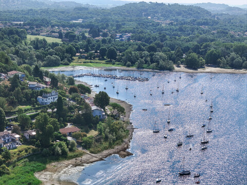 Aerial view of Sasso Moro and the coastline of Lake Maggiore with sailboats moored in the bay, lush trees, and houses in Leggiuno, Lombardia, Italy.