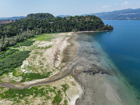 Aerial view of Lake Maggiore showing the exposed shoreline and receding water levels during a summer drought in Monvalle, Lombardy, Italy.
