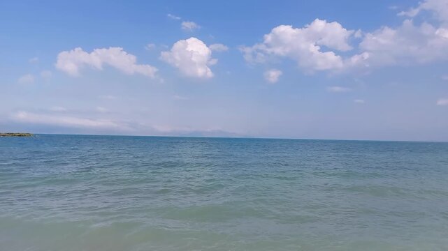 Beautiful calm blue water of Lake Sevan with fluffy white clouds in Armenia. Peaceful wide view of calm blue water surface and gentle ripples on Lake Sevan under bright sunny sky with fluffy white clo