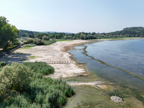 Aerial view of the receding shoreline of Lake Maggiore during a severe drought, showing exposed dry lakebed, sparse vegetation, and low water levels in Monvalle, Lombardy, Italy.