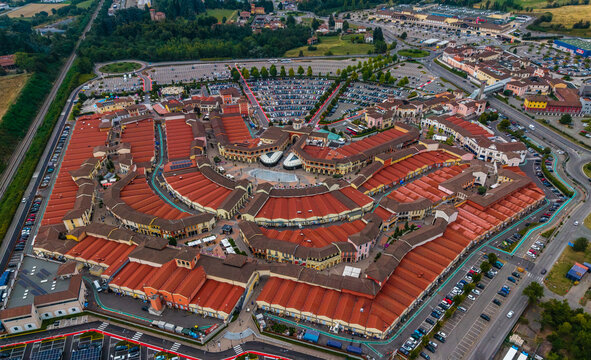 Aerial view of Designer Outlet Serravalle with its distinctive red-tiled roofs, central plaza, and surrounding parking areas in Serravalle Scrivia, Piemonte, Italy.