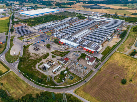 Aerial view of the Roquette plant featuring large industrial buildings with solar panels, parking areas, and adjacent agricultural fields in Serravalle Scrivia, Piedmont, Italy.