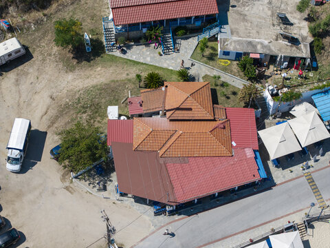 Aerial view of Sykias Beach featuring a building with a red tiled roof, surrounding coastal landscape, and nearby beach umbrellas in Paralia Sikias, Greece.