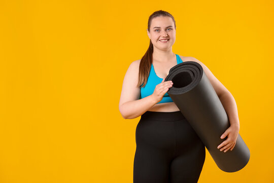 Happy overweight woman with fitness mat on yellow background, space for text