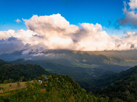Aerial view of Mount Agung surrounded by lush green tropical forests, rolling hills, and dramatic clouds in the sky in Bebandem, Bali, Indonesia.