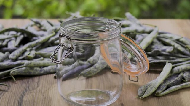 Open swing-top jar on wooden table with green beans and leaves background, 4K