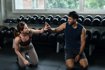 Fototapeta premium Young Asian couple celebrates partner workout with high five on modern gym floor, man and woman sharing motivation, teamwork, encouragement, healthy relationship, bodyweight strength lifestyle.