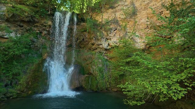 Water cascades down rocky cliff into serene pool. Veliki Buk, Serbia.