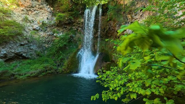 Lush green leaves frame a cascading waterfall. Veliki Buk, Serbia.