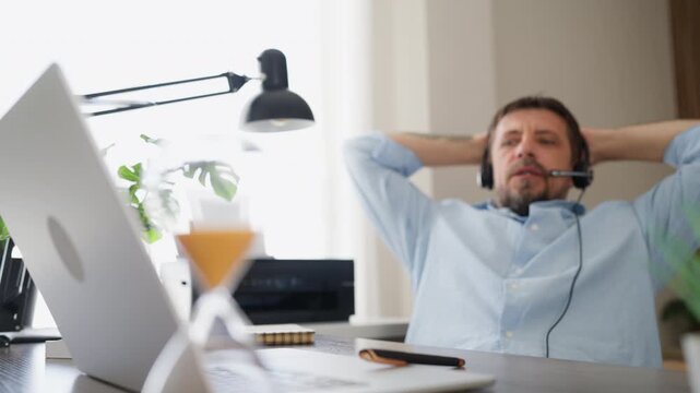 Confident businessman leaning back in office chair while speak through headset during an online business conversation. Professional communication, remote work, leadership,workplace confidence concept
