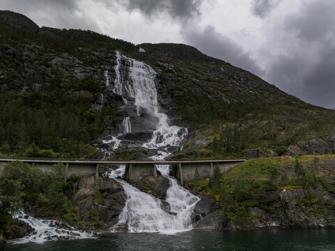Aerial view of Langfoss waterfall cascading down a rocky mountainside with a bridge crossing the stream under a cloudy sky in Fjaera, Vestland, Norway.