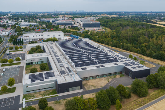 Aerial view of the Poly-clip System GmbH Co. KG facility featuring extensive solar panels on the roof, surrounded by parking areas and green spaces in Hattersheim am Main, Hessen, Germany.