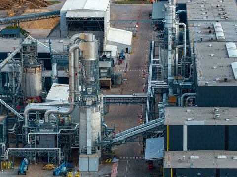Aerial view of a wood processing installation with industrial silos, metal piping, and conveyor belts at a manufacturing facility in Poland.