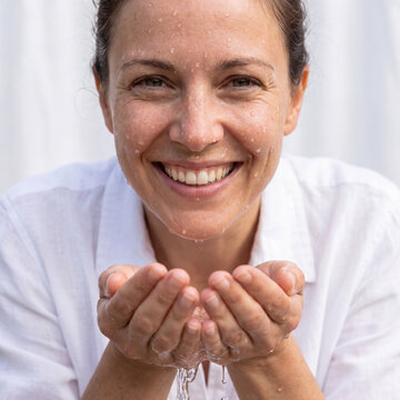 Mature woman smiling broadly while splashing water from cupped hands in fresh morning routine