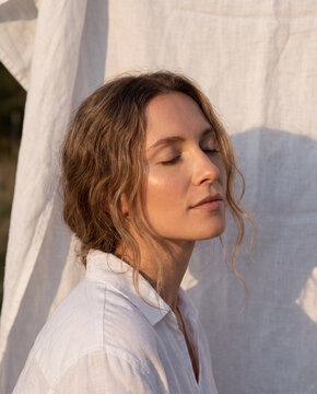 Profile of woman with blonde hair in white linen shirt bathed in warm golden hour backlight