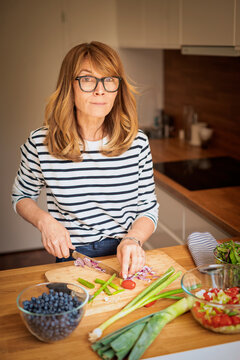 Mid-aged woman chopping fresh vegetables on a wooden cutting board in a modern kitchen