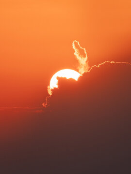 Aerial view of the sun setting behind clouds in the orange sky.