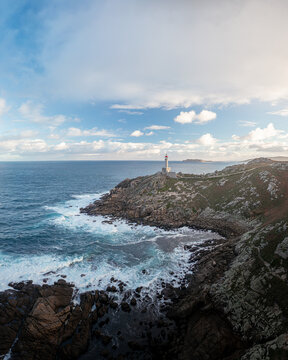 Aerial view of Faro de Punta Nariga lighthouse perched on rugged granite cliffs with white waves crashing against the rocky shore Malpica, A Coruna, Spain.