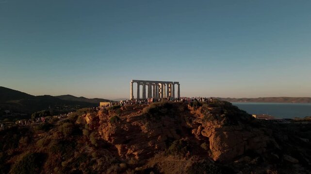 Sounion, Greece - 01 June 2026: Aerial view of the ancient Temple of Poseidon on a rocky cliff with tourists gathered at sunset.