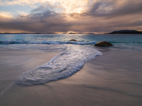 View of Frenchman Bay with gentle waves washing over the white sand beach under a dramatic cloudy sky at sunset, Frenchman Bay, Western Australia, Australia.