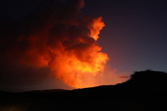 View of Fagradalsfjall Volcano erupting at night with glowing lava plumes rising into the dark sky in Grindavik, Grindavikurbaer, Iceland.