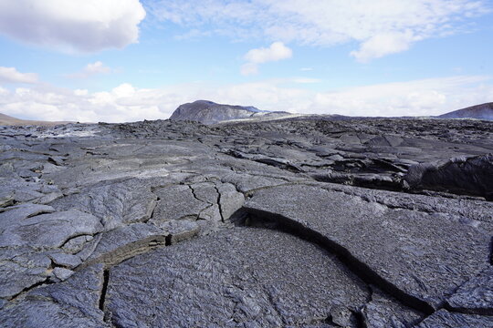 View of the solidified lava field at Fagradalsfjall Volcano with cracked dark volcanic rock formations under a blue sky in Grindavik, Grindavikurbaer, Iceland.