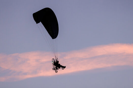 View of a paramotor silhouette flying against a soft pink and purple sunset sky in Poland.