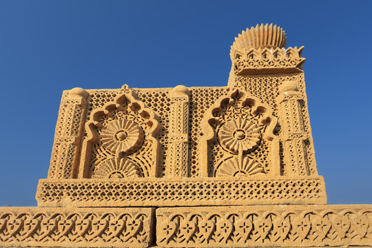 View of the intricately carved sandstone Chaukhandi tombs featuring geometric patterns and floral motifs under a clear blue sky in Karachi, Sindh, Pakistan.