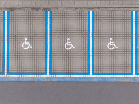 Aerial view of three marked handicap parking spaces with blue lines on paved ground in Diepenbeek, Belgium.