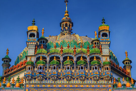 View of the ornate and colorful Shrine of Sachal Sarmast featuring intricate tile work, decorative domes, and minarets against a clear blue sky in Daraza Sharif, Sindh, Pakistan.