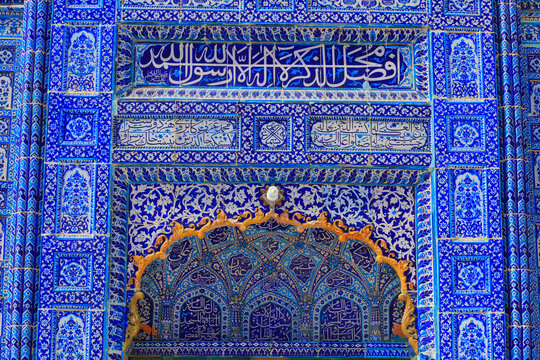 View of Kamaro Sharif Mosque featuring intricate blue and white glazed tile work with detailed Islamic calligraphy and ornate golden arches in Kaamaro Sharif, Sindh, Pakistan.