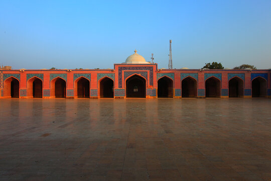 View of the historic Shah Jahan Masjid featuring red brick arches, intricate blue tile work, and a central dome under a clear sky in Thatta, Sindh, Pakistan.