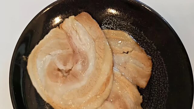Roasted chashu pork belly roll slices on a plate, Ramen Topping, Japanese Food Cuisine, Meat Roast, Slow Motion Panning Overhead Shot