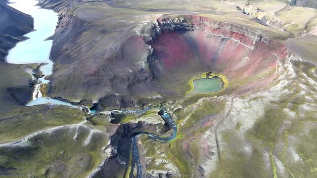 Aerial view of the volcanic crater Raudibotn with its red slopes, a small crater lake, and winding river channels in Svartafellstangi, Skaftarhreppur, Iceland.