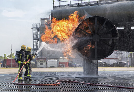 View of two firefighters in protective gear using a hose to extinguish a controlled fire on a large metal training structure at Sloterweg 527 in Badhoevedorp, Noord-Holland, Netherlands.