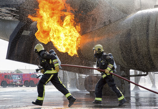 View of two firefighters in protective gear running with a fire hose towards a controlled fire during a training exercise at Sloterweg 527 in Badhoevedorp, Noord-Holland, Netherlands.