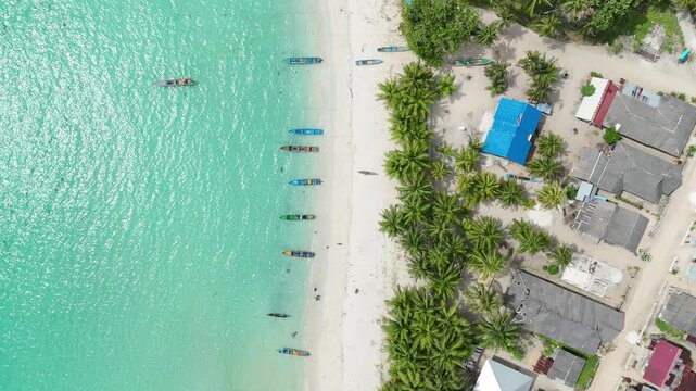 Aerial view of Pantai Ohoidertutu Ngur Mun Vat Wahan with turquoise water and traditional boats along the white sand beach in Kei Kecil Barat, Maluku, Indonesia.