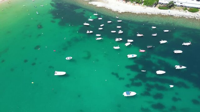 Aerial view of numerous small boats anchored in the clear turquoise waters of the bay in Port de Soller, Balearic Islands, Spain.