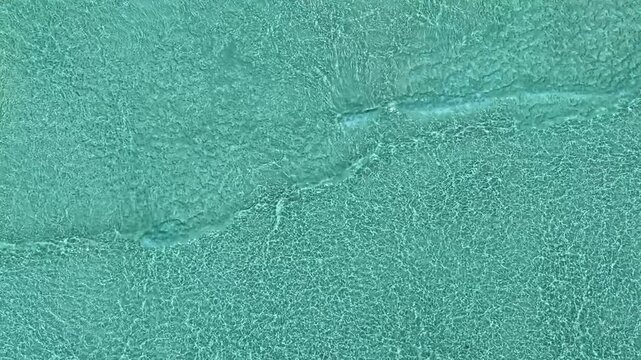 Aerial view of crystal clear turquoise ocean water with gentle ripples washing over the sandy seabed in Vashafaru, Haa Alif Atoll, Maldives.