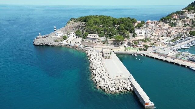 Aerial view of Port de Soller harbor with its iconic lighthouse, breakwater, and docked boats along the Mediterranean coast in Port de Soller, Balearic Islands, Spain.