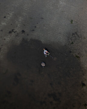 Aerial view of a fisherman harvesting clams in shallow water with a rake and a bucket in Carril, Pontevedra, Spain.