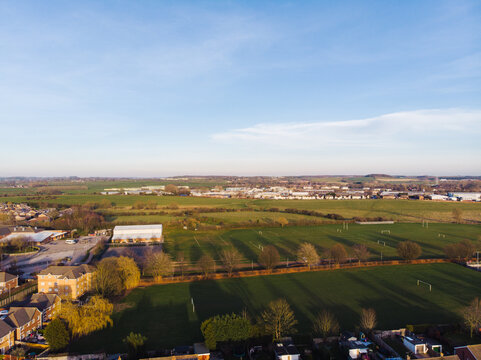Aerial view of green fields, sports pitches, and residential buildings in the outskirts of Stafford, England, United Kingdom.