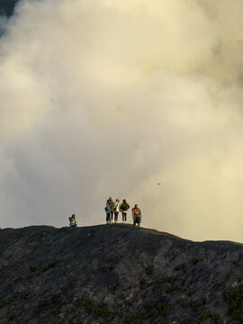 Aerial view of Mount Bromo with a group of people standing on the volcanic ridge against a backdrop of thick volcanic smoke in Tosari, East Java, Indonesia.