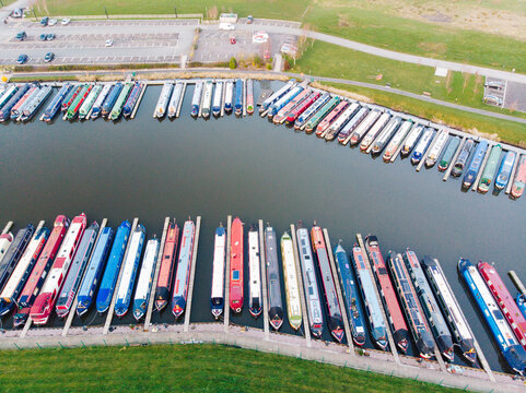 Aerial view of Aston Marina with colorful narrowboats moored in orderly rows along the canal docks, surrounded by grassy banks and a parking area in Stone, England, United Kingdom.