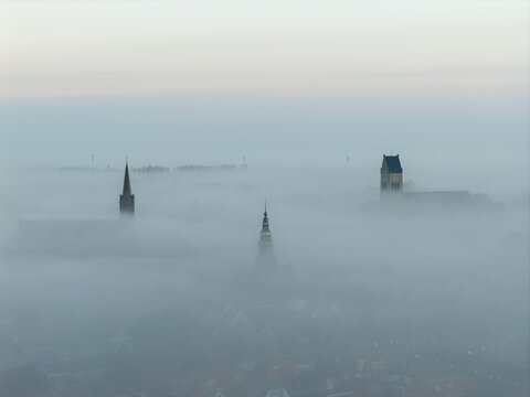 Aerial view of the historic church towers of Bolsward rising above a thick layer of morning fog in the city center of Bolsward, Friesland, Netherlands.