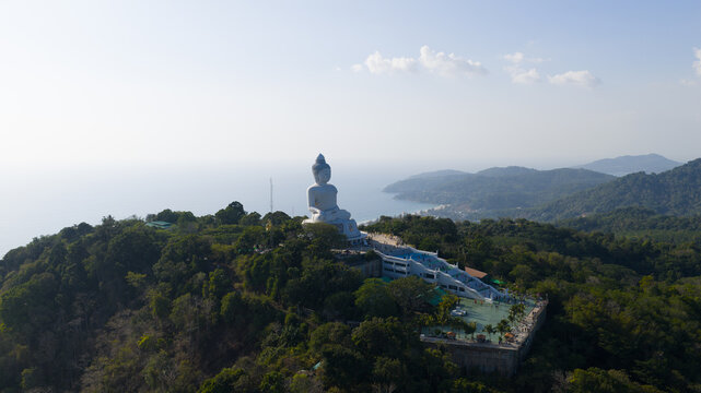 Aerial view of the Big Buddha Phuket statue situated on a lush hilltop overlooking the coastline and sea in Karon, Phuket, Thailand.