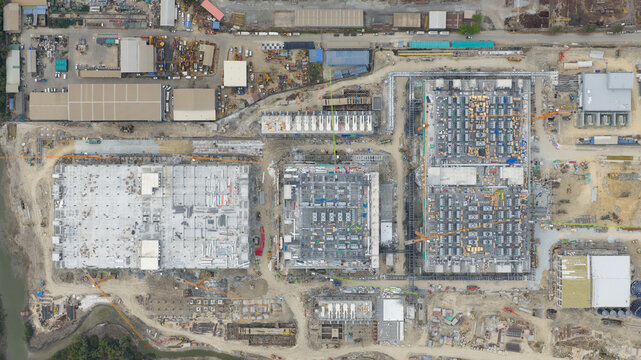 Aerial view of the Bridge Data Center construction site featuring industrial buildings, heavy machinery, and cranes in an expansive development area in Khlong Tamru, Chon Buri, Thailand.